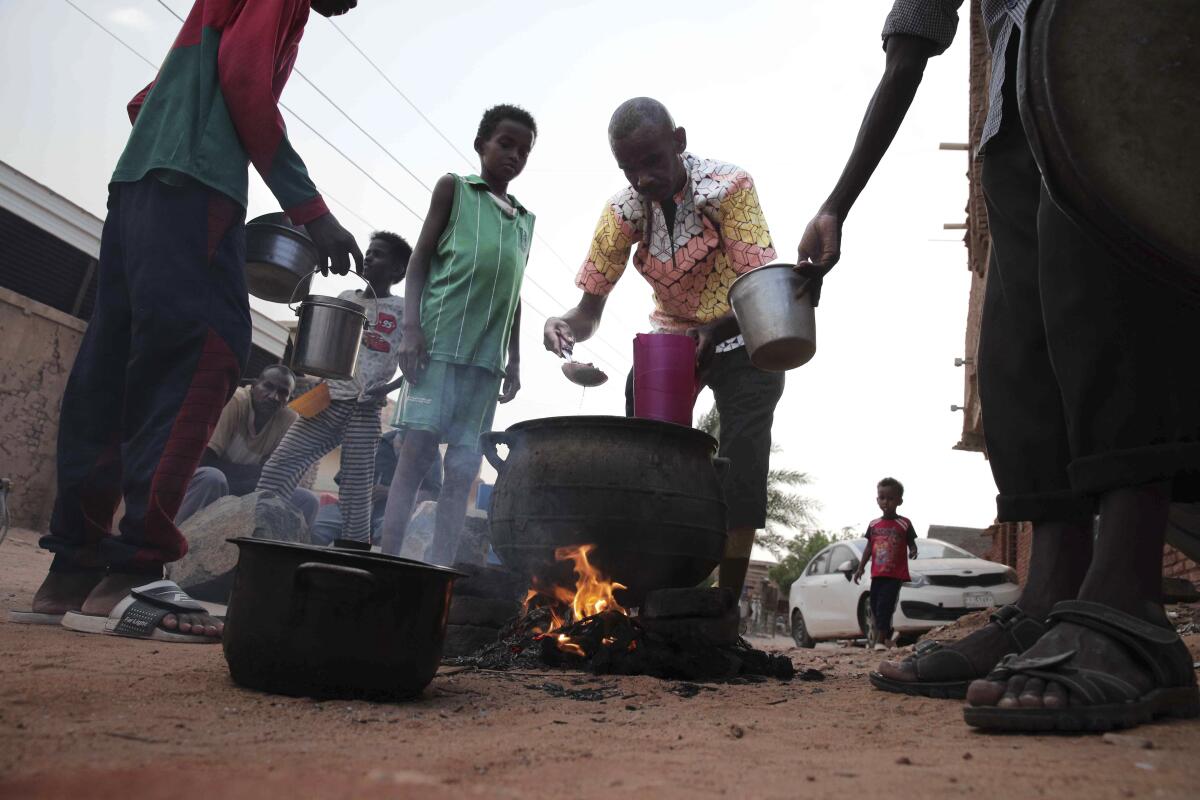 A man dishes out food from a big pot on a fire outdoors.
