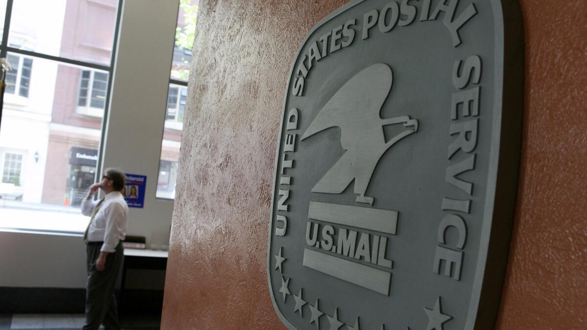 A file photo shows a man walking by a sign in the lobby of a post office. A Santa Ana postal worker was accused of stealing thousands of credit cards.