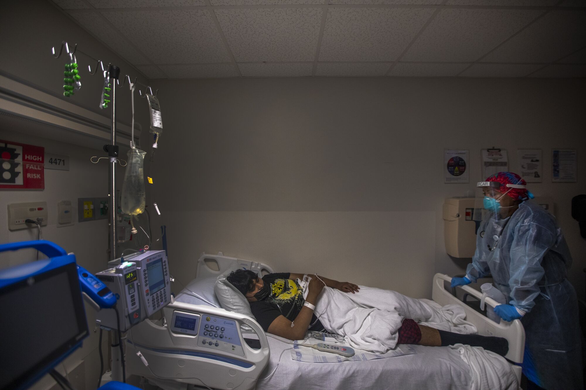 A doctor in protective gear stands over the bed of a patient