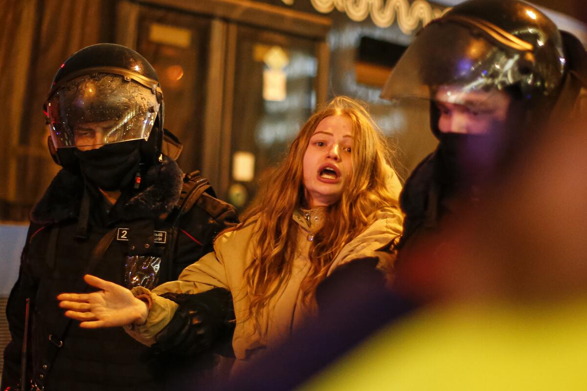 Two officers in riot gear hold the arms of a woman.