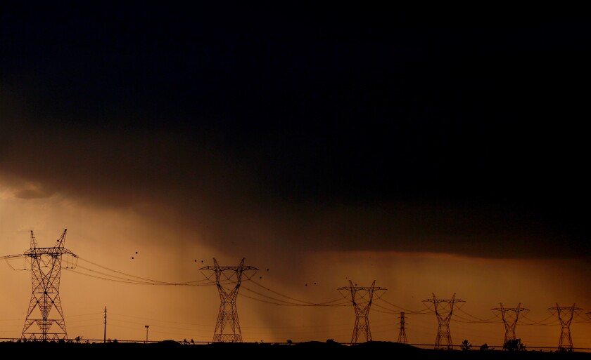 Rain falls behind power lines near Adelanto at the end of a scorching hot day Wednesday.
