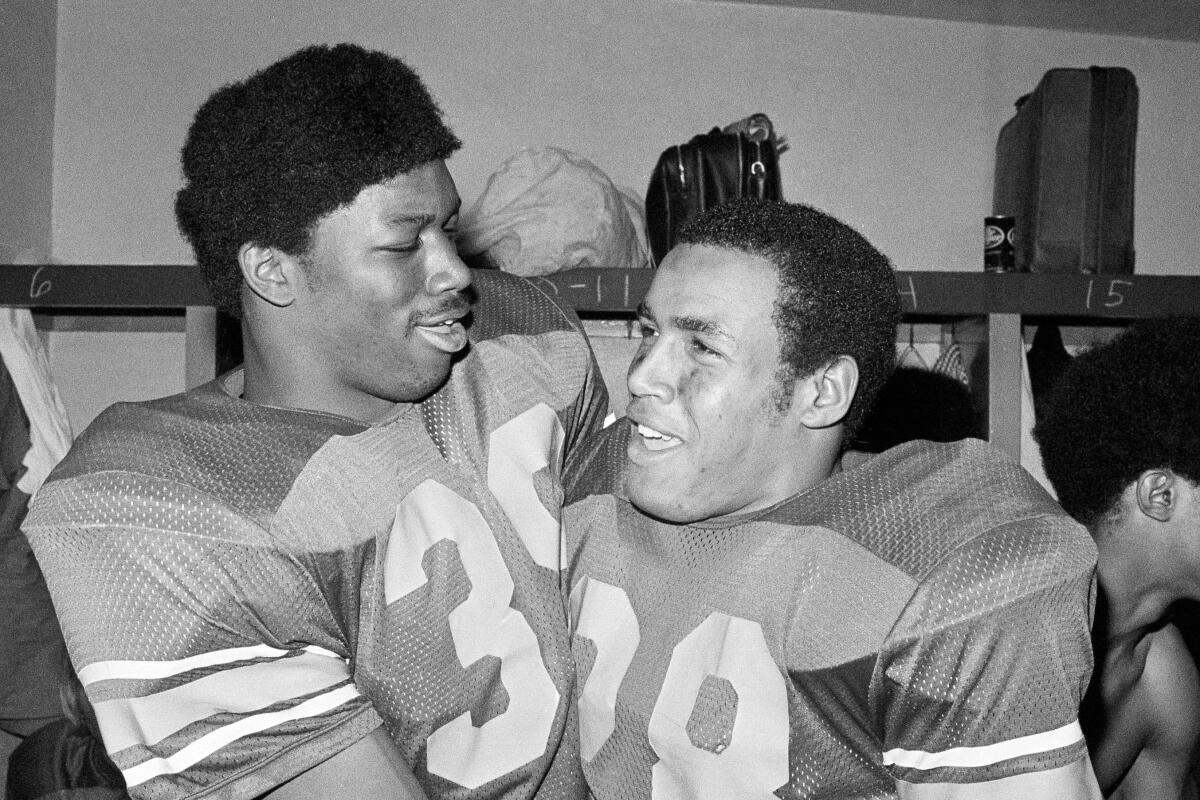 FILE - In this Jan. 1, 1973, file photo, Southern California fullback Sam Cunningham, left, and running back Anthony Davis embraces in locker room after USC.s 42-17 triumph in the Rose Bowl NCAA college football game against Ohio State in Pasadena, Calif. Cunningham, an All-American fullback at Southern California whose performance against Alabama was credited for helping integrate football in the Deep South before he went on to a record-setting career with the New England Patriots, died Tuesday, Sept. 7, 2021, at his home in Inglewood, Calif., according to USC. He was 71. (AP Photo/File)