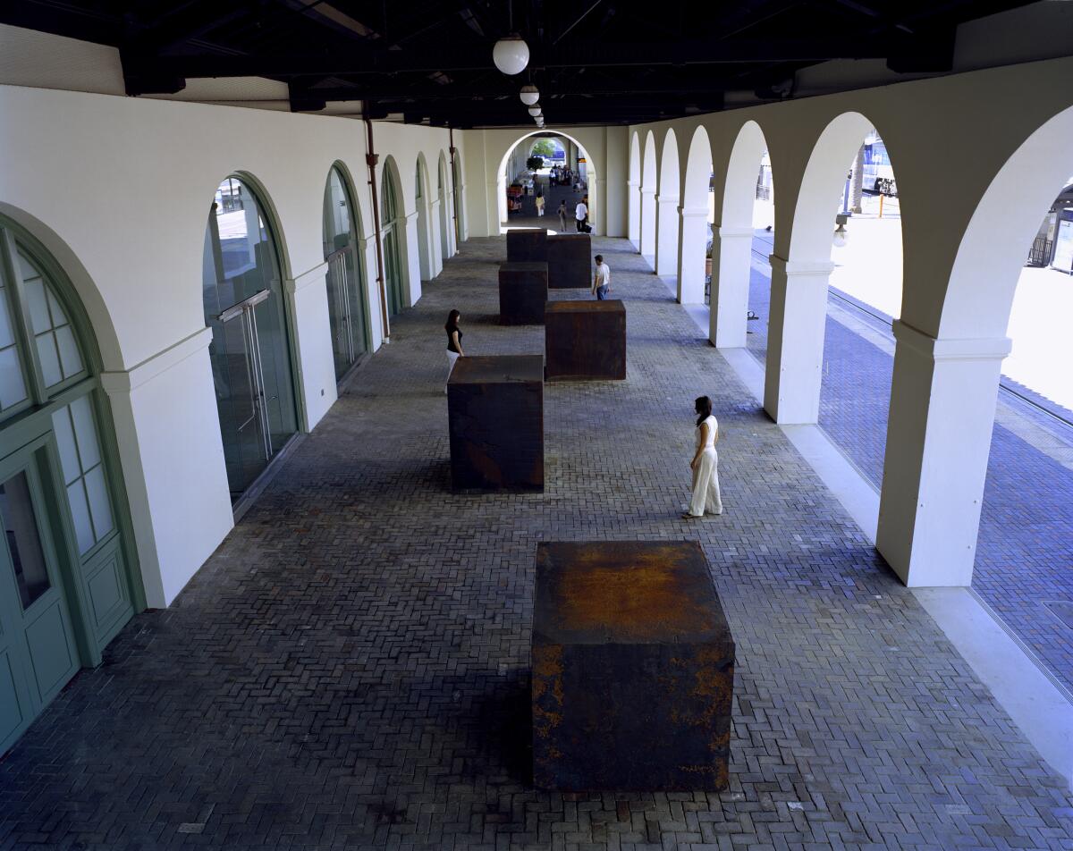 Six cube-like steel structures are staggered in a corridor with arches.