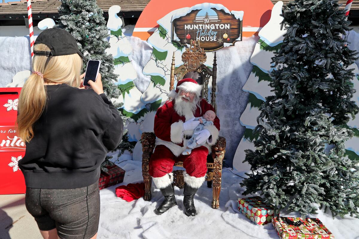 Huntington Beach resident Simone Parmenter, left, takes a photo of her 2-month-old son, Beau, with Santa Claus on Friday.