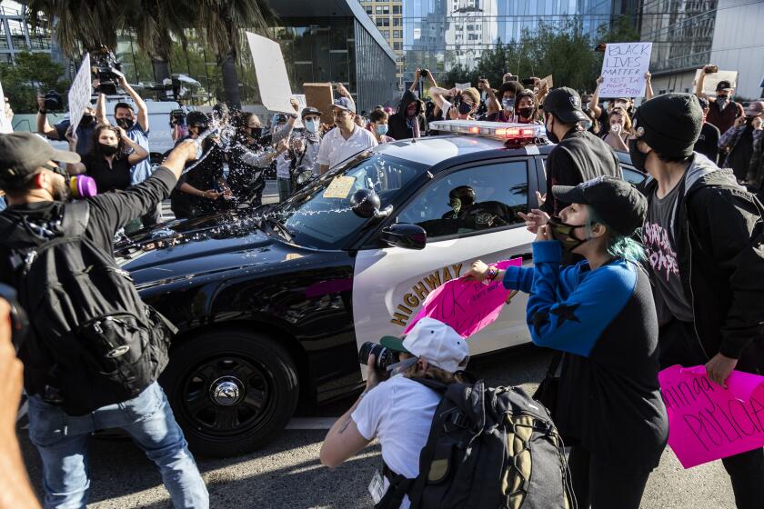 LOS ANGELES, CA - MAY 28, 2020: A protester tosses a bottled water on a CHP vehicle as other Black Lives Matter protesters swarm the car in a rally in front of LAPD headquarters to protest the death of George Floyd during the coronavirus pandemic on May 28, 2020 in Los Angeles, California. (Gina Ferazzi / Los Angeles Times)