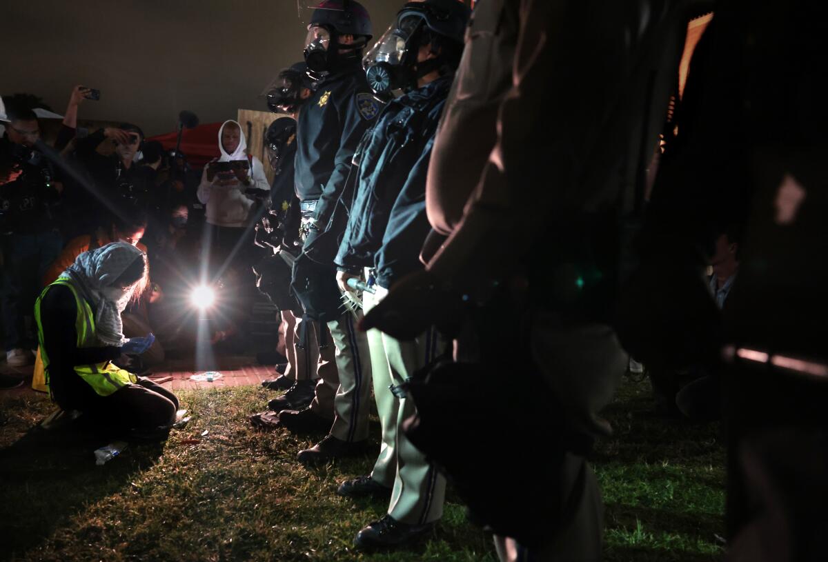 A woman kneels in prayer in front of a line of law enforcement officers.  