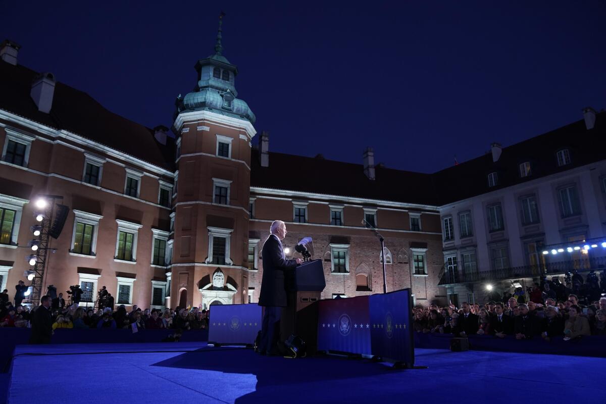 President Biden speaks at a lectern before guests seated around him in a courtyard, with buildings as a backdrop