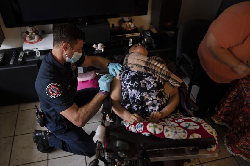 Torrance firefighter Trevor Borello, left, administers the second dose of the Pfizer COVID-19 vaccine to Barbara Franco, who suffers from muscular dystrophy, at her apartment, Wednesday, May 12, 2021, in Torrance, Calif. Teamed up with the Torrance Fire Department, Torrance Memorial Medical Center started inoculating people at home in March, identifying people through a city hotline, county health department, senior centers and doctor's offices, said Mei Tsai, the pharmacist who coordinates the program. (AP Photo/Jae C. Hong)
