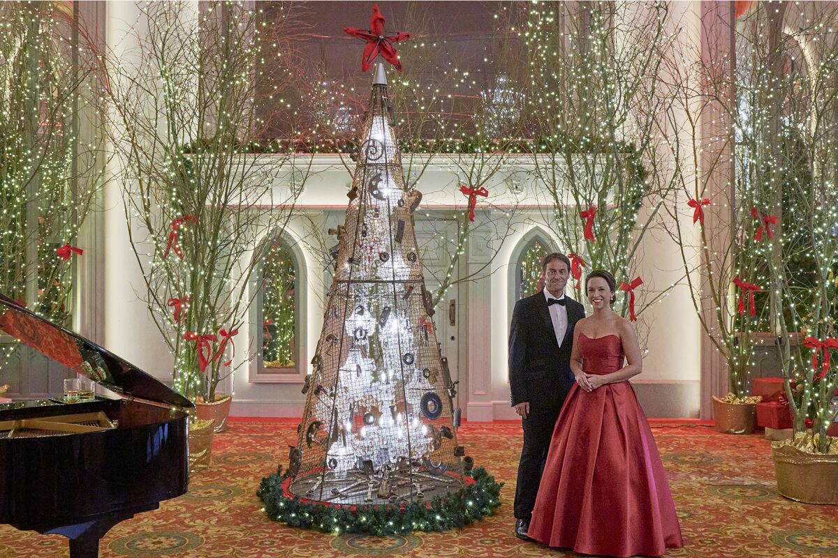 A man and a woman in formal wear stand in a room lavishly decorated for Christmas.