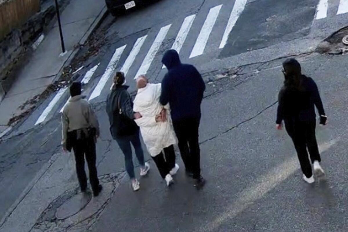 A young woman is detained by Department of Homeland Security agents on a street.