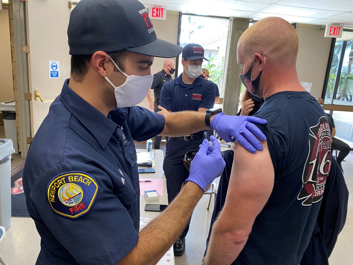 Newport Beach paramedic Joel Chidley, left, administers a vaccine to a paramedic for the Costa Mesa Fire Department.