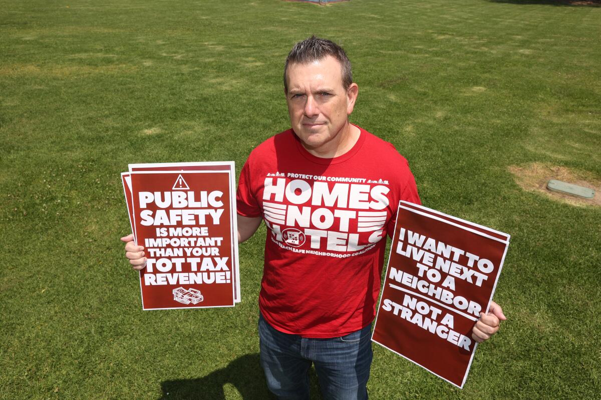A man stands on a lawn in a T shirt that reads "Homes not hotels."
