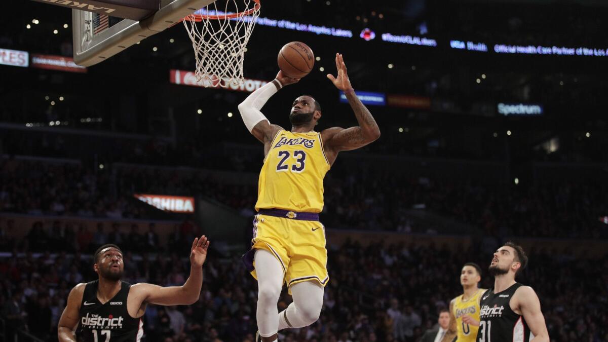 Lakers' LeBron James, center, goes up for a dunk as Washington Wizards' Jabari Parker, bottom left, and Tomas Satoransky look on during the first half on Tuesday at Staples Center.