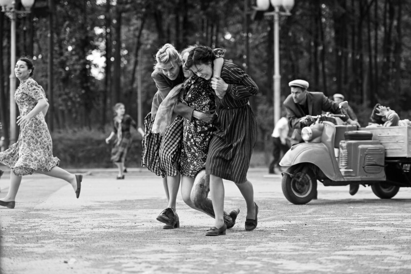 Two women half-carry a wounded woman on the street.