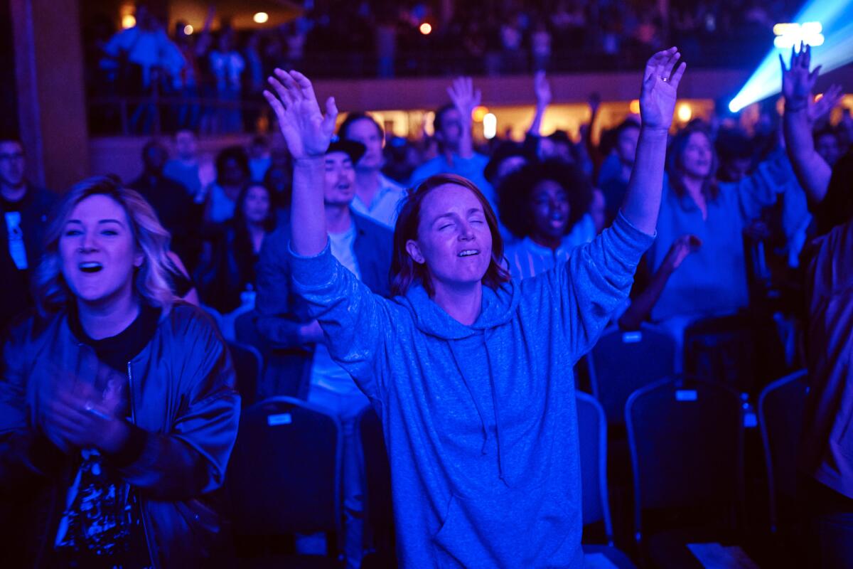 Worshipers raise their arms and sing at a large Pentecostal service. 