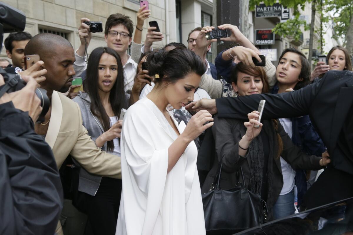 People gather around Kim Kardashian, center, and Kanye West, left, as they leave their residence in Paris on May 23, 2014, ahead of their wedding.