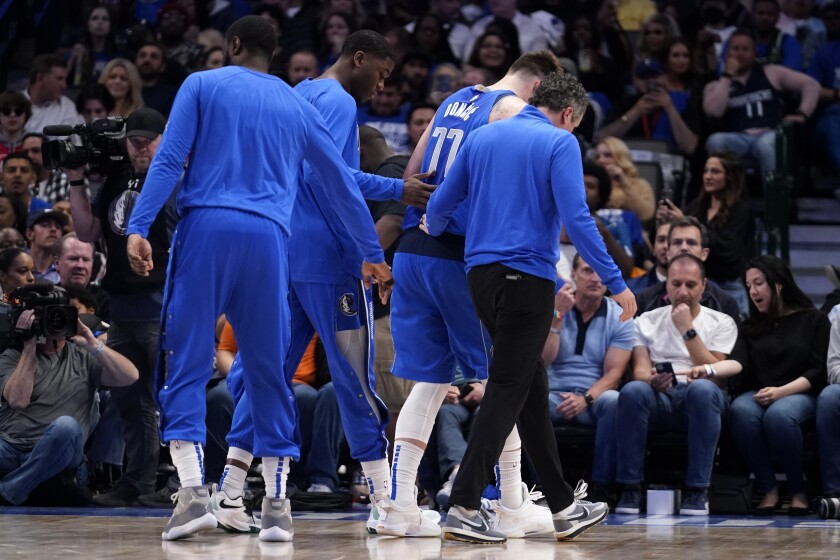 Dallas Mavericks guard Luka Doncic is helped off the court by teammates and a member of the staff after suffering an unknown lower leg injury in the second half of an NBA basketball game against the San Antonio Spurs, Sunday, April 10, 2022, in Dallas. (AP Photo/Tony Gutierrez)