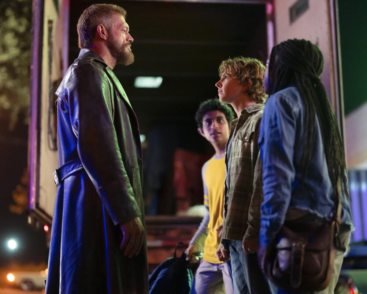 A man in a black trench coat looks at three children in front of him.