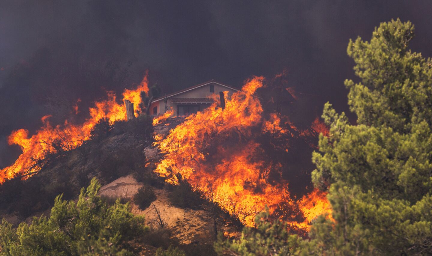 A house is surrounded by flames as the Blue Cut Fire roars above Highway 138 in Phelan, Calif., on Tuesday.