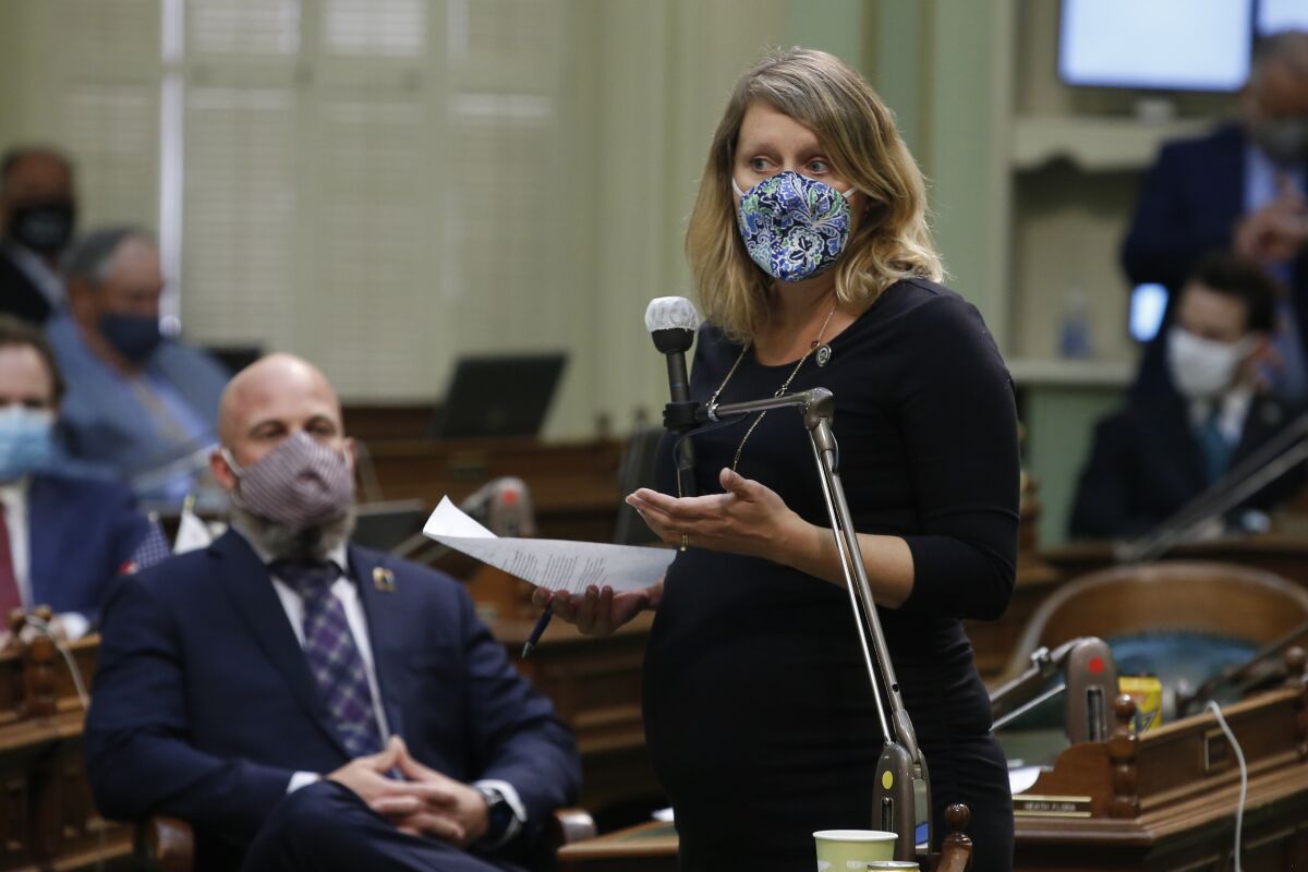 A woman wearing a face mask stands at a microphone.