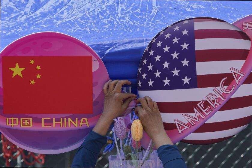 Un comerciante ata unas flores decoragivas entre dos banderas de China y Estados Unidos con forma de planeta, en una tienda durante el Carnaval de Primavera en Beijing, el 13 de mayo de 2023. (AP Foto/Andy Wong)