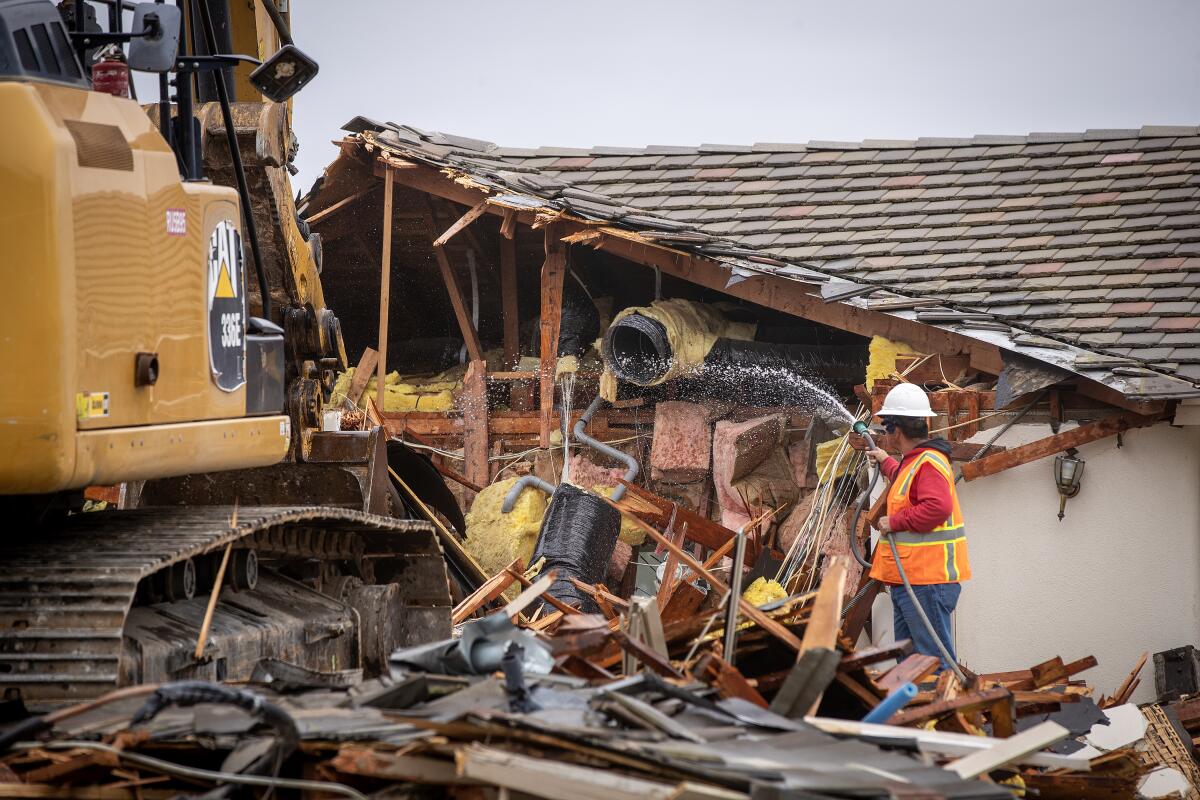 The side of a house is missing as workers use a bulldozer to tear it down.