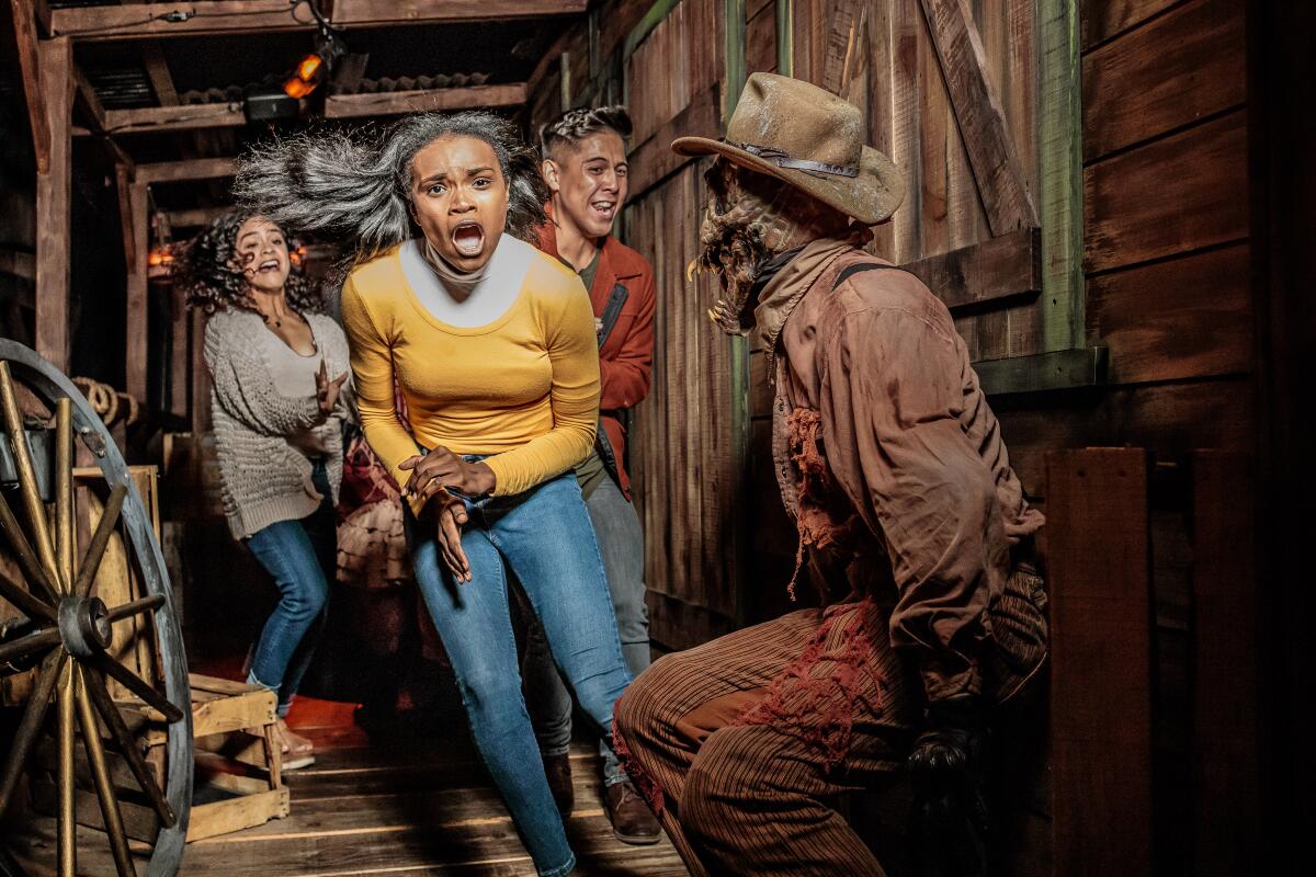 A screaming woman with a frightened expression runs past an actor dressed as a scarecrow in a Halloween horror maze.