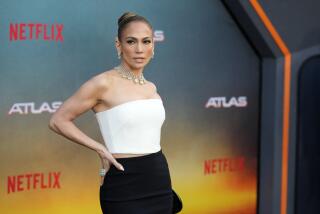 Jennifer Lopez in a white white and black strapless gown posing with her hands on her hips at a red carpet event