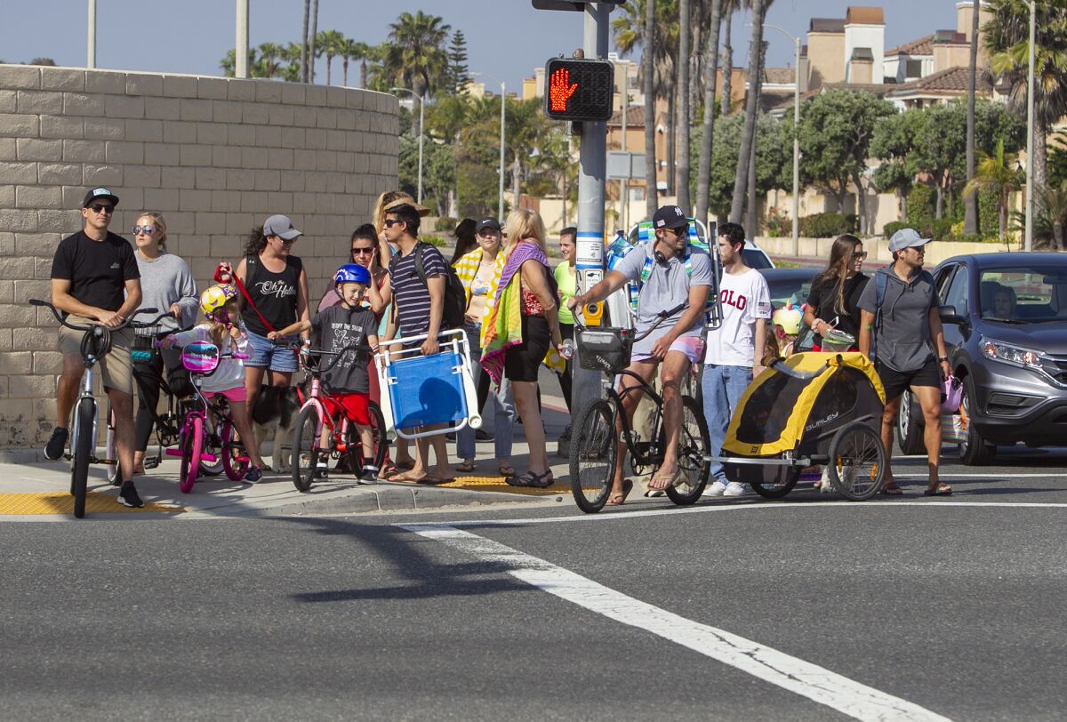 A crowd of people gather to cross the street on their way to the beach at the corner of Pacific Coast Highway and Goldenwest Street in Huntington Beach on Thursday.