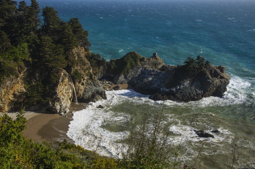 Aerial view of a rocky beach inlet with water flowing from a cliffside.