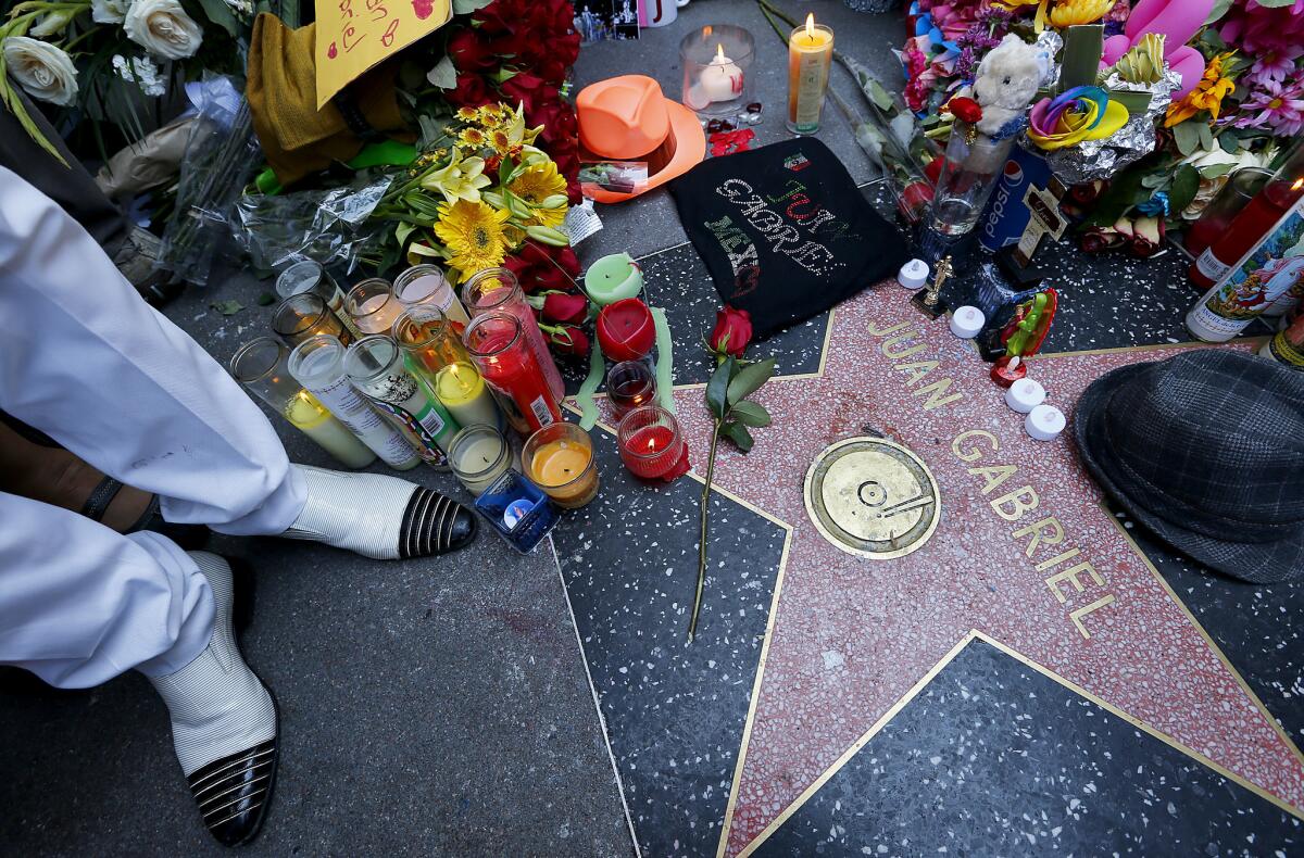 A fan of Mexican pop singer-songwriter Juan Gabriel stands next to his star on the Hollywood Walk of Fame, which was turned into an impromptu memorial. Juan Gabriel died Sunday at age 66.