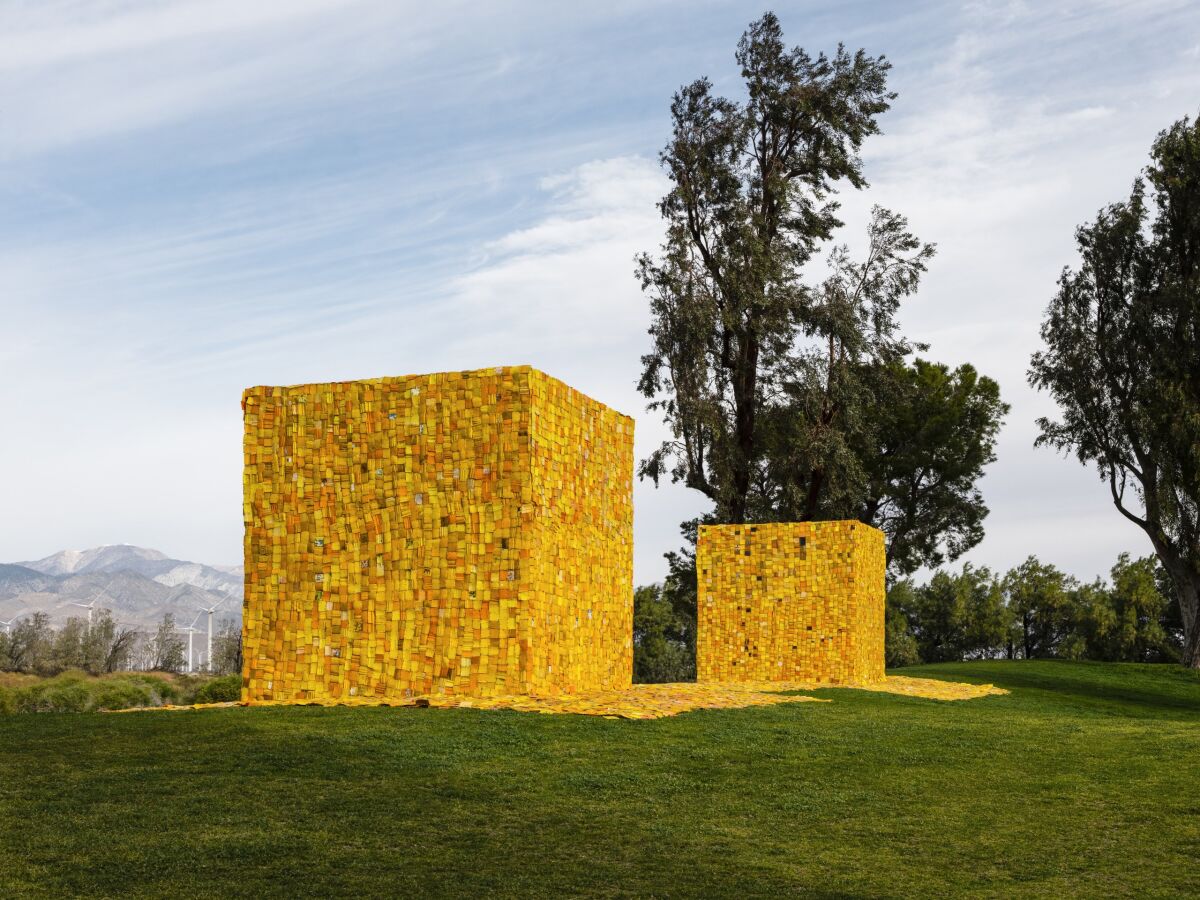 Two yellow cubes made of small yellow plastic squares sit on a green hilltop