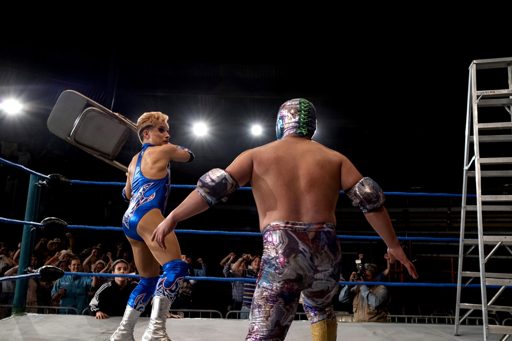 A wrestler in blue swings a chair at another on the canvas.