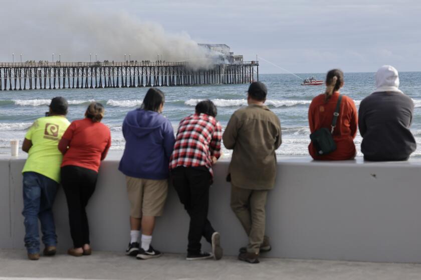 People watch as fire crews fight a fire burning at the end of the Oceanside Municipal Pier.