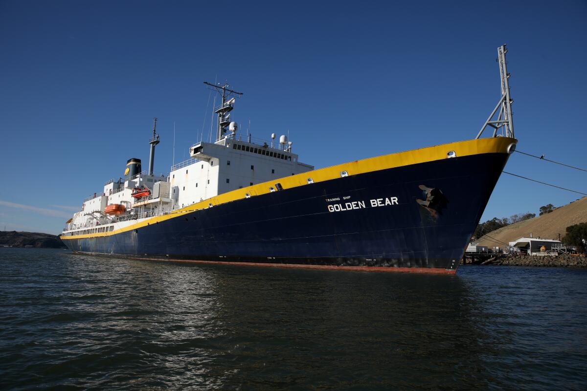 A 500-foot training ship docked near shore with 'Golden Bear' stenciled in capital letters on its navy and gold hull 