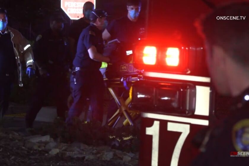 A police officer watches as paramedics roll a gurney carrying a man who was shot by police Friday night in City Heights.