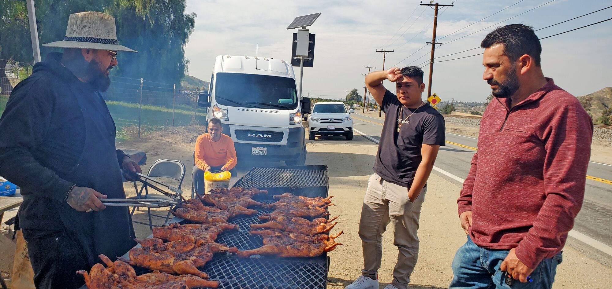 Customers watching as man grills chickens at a roadside stand 
