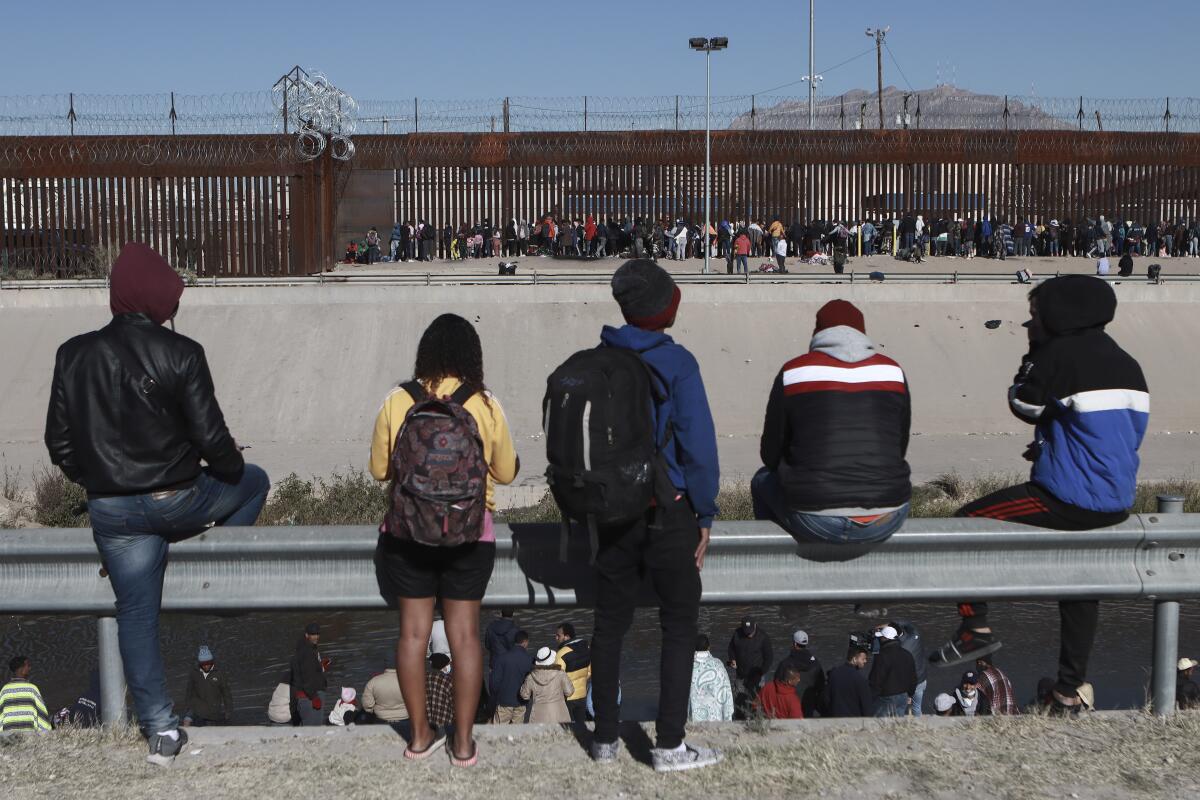 Archivo - Varios migrantes observan a otros junto a la valla fronteriza en Ciudad Juárez, México,