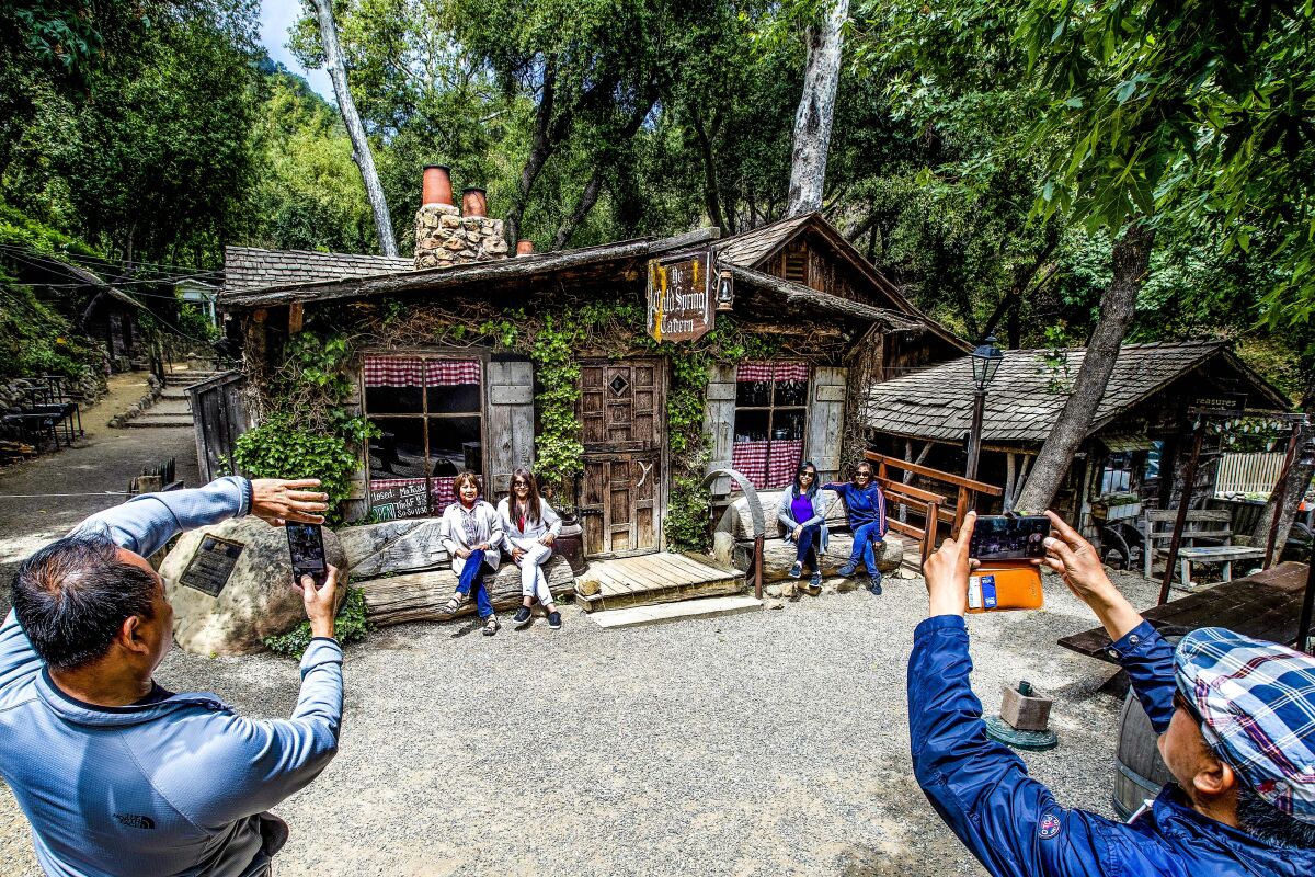 People take photos of a quaint stone and wood building with people sitting out front on benches.