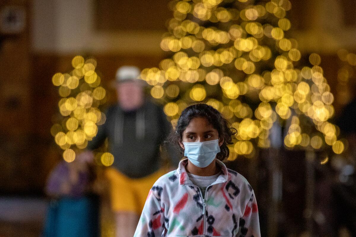 A young commuter walks through Los Angeles Union Station while wearing a mask.