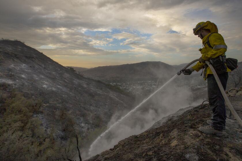 LA County firefighter Kevin Sleight extinguishes hot spots while battling the La Tuna Canyon fire along Crestline Drive Sunday.