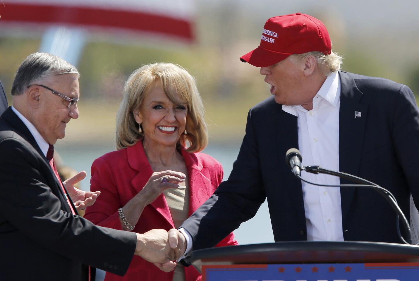 Maricopa County Sheriff Joe Arpaio, left, and former Arizona Gov. Jan Brewer greet Republican presidential candidate Donald Trump at a rally in Fountain Hills, Ariz., on Saturday. Arpaio and Trump have a hard line on immigration. Latinos and immigrants' rights advocates held protests. Arizona's primary is Tuesday.