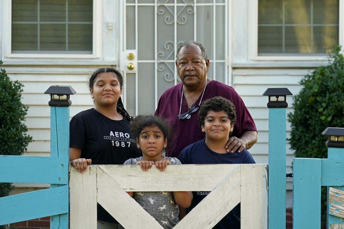 A man poses with his three grandchildren outside his home.