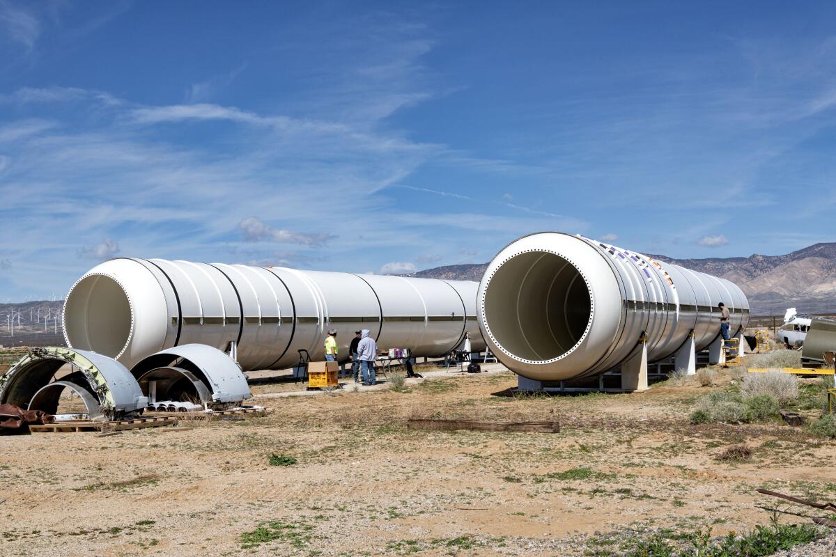 People stand in between two rocket motors sitting on stands. 