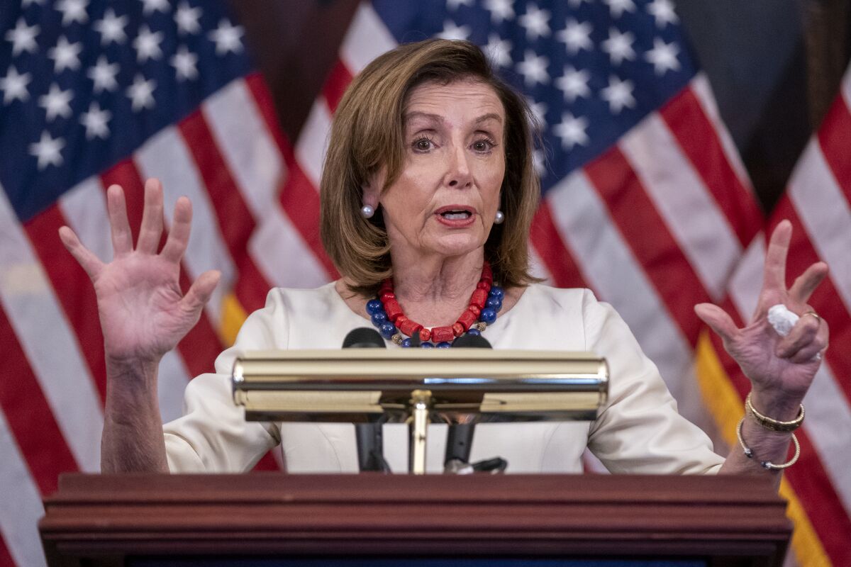 House Speaker Nancy Pelosi gestures as she speaks against a background of American flags
