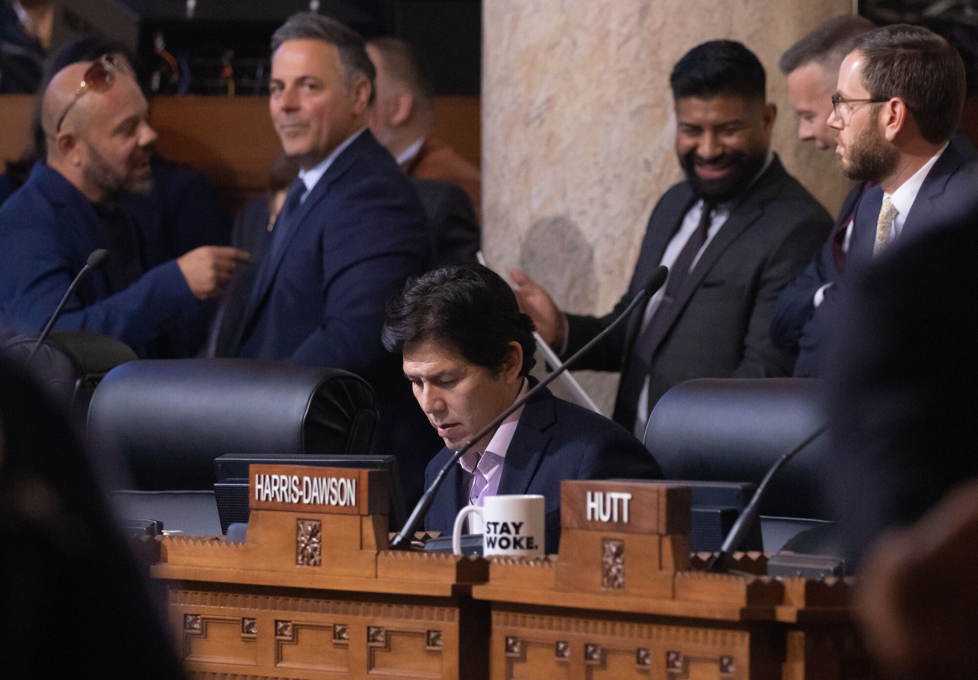 Los Angeles City Council Member Kevin de León sits while other people talk and move behind him.