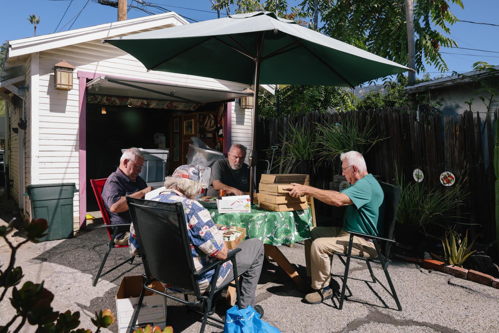People sit at a table under a big umbrella, outside an open garage, sorting through matchbooks