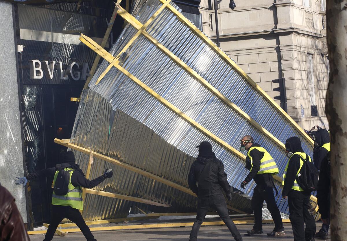 Protesters tear down a protective wall in front of a luxury shop during a demonstration in Paris.