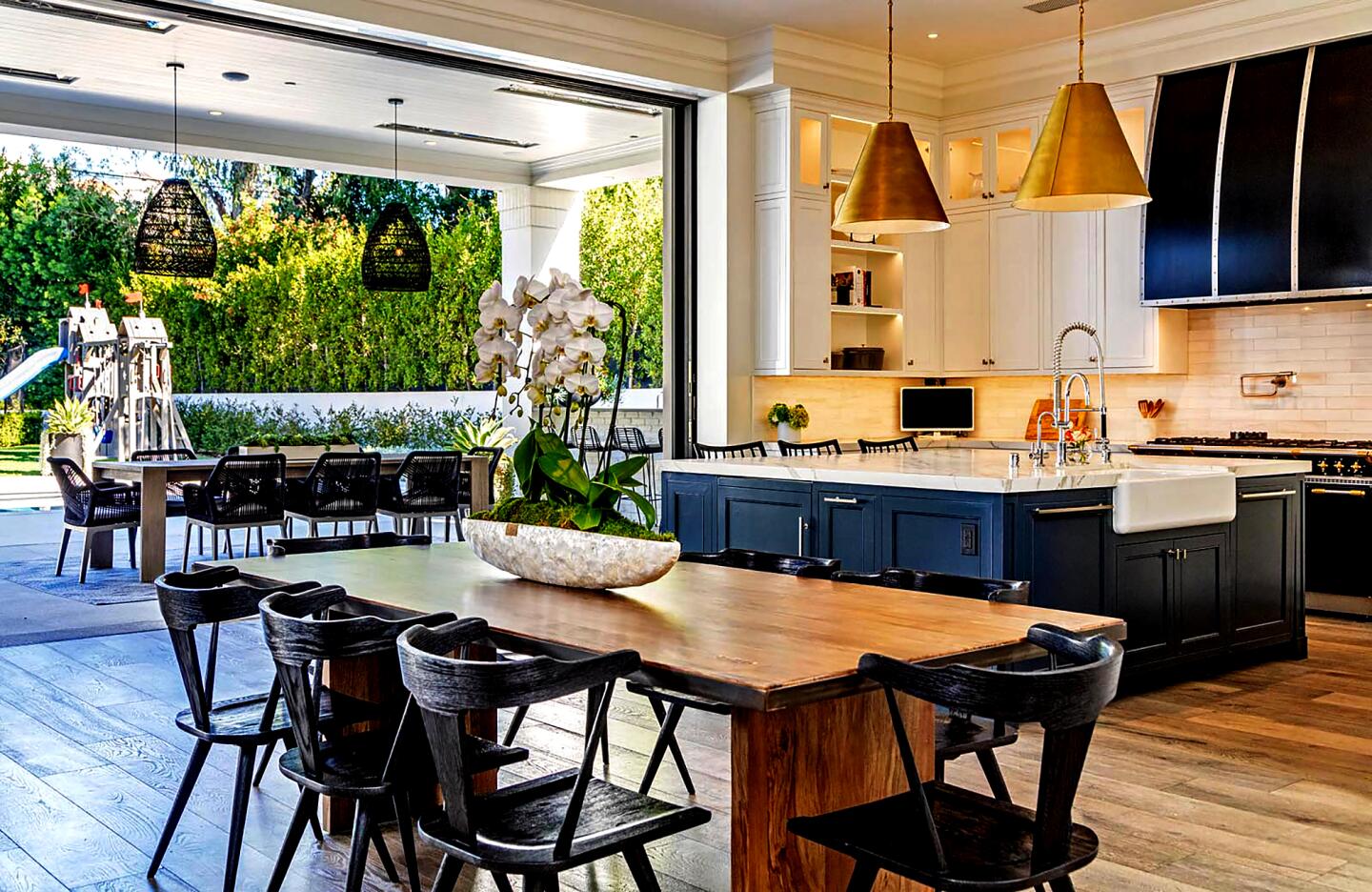 The kitchen with appliances, a dining set, an island and chairs overlooking an outdoor dining set and landscaping.