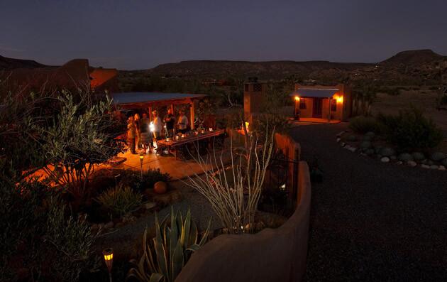 By David A. Keeps Friends gather by the flowing garden fireplace and outdoor dining table of the pueblo-style residence, whose generous patio spaces easily accommodate two-dozen. The guest house is on the right.